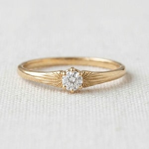 Peut inclure: Une bague en or avec une pierre précieuse transparente ronde taille brillant sertie au centre. L'anneau est fabriqué en or jaune poli et présente un motif gravé en forme de rayons de soleil partant du sertissage de la pierre centrale.