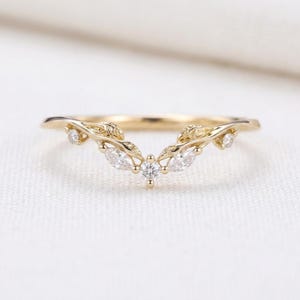 Puede incluir: Un anillo de oro en forma de V con un delicado diseño de banda inspirado en hojas. El anillo está engastado con cinco piedras claras y brillantes, incluyendo una piedra redonda central, dos piedras talla marquesa y dos piedras redondas.