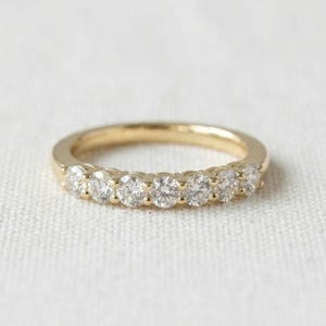Peut inclure: Une bague en or avec sept pierres rondes transparentes serties en ligne sur la moitié supérieure de l'anneau. Le métal présente une finition en or jaune poli et les pierres sont disposées symétriquement pour un effet brillant continu.