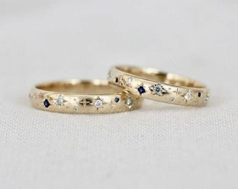 May include: Two gold rings featuring a celestial motif with flush-set clear white stones and small dark blue stones. The bands are decorated with engraved starburst patterns and tiny dots, creating a starry night sky effect across the metal surface.