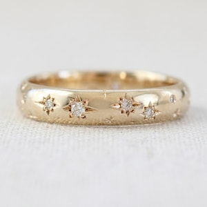 Peut inclure: Une bague anneau en or avec une finition polie et de multiples gravures en forme d'étoile. Chaque étoile est centrée par une petite pierre précieuse ronde et claire. Le design inclut un mélange de motifs d'étoiles et de gravures simples.