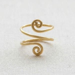 May include: A gold-toned metal ring featuring a continuous spiral design. The band wraps around to form two distinct circular coils at each end, creating an open-ended structure with a matte finish and a smooth, rounded wire construction.