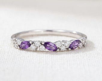 May include: A silver-toned ring featuring a thin band set with three marquise-cut purple amethyst stones alternating with clusters of small, round, clear white stones arranged in a horizontal row across the front of the band.