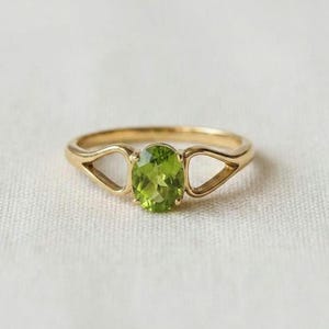May include: A gold ring featuring a central oval-cut lime green peridot gemstone held by four prongs. The band is crafted from polished yellow gold and includes a distinctive open triangular design on each side of the central stone setting.