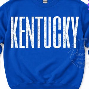 May include: A royal blue crewneck sweatshirt featuring the word KENTUCKY printed in large, white, distressed capital letters across the chest. A purple starburst graphic in the top right corner contains the text Digital File.