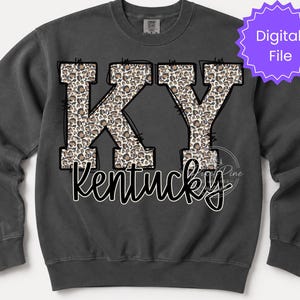 Peut inclure: Un sweat-shirt à col rond gris anthracite arborant les lettres KY dans un motif imprimé léopard marron et noir avec un contour noir. Sous les lettres, le mot Kentucky est écrit en police cursive blanche avec un contour noir.
