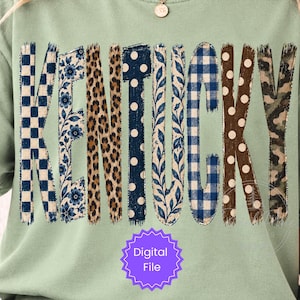 May include: A sage green t-shirt featuring the word KENTUCKY in large block letters. Each letter displays a different pattern, including blue and white checkerboard, blue floral, leopard print, navy polka dots, blue gingham, and camouflage.