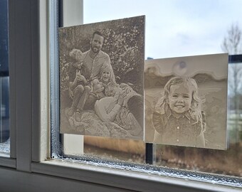 May include: Two sepia-toned photographs are displayed on a window. The first photo shows a family of four, a man, a woman, and two children. The second photo shows a young girl with a bright smile.