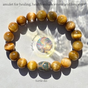 Könnte beinhalten: Ein goldgelbes Perlenarmband mit einer Schildkröten-Dzi-Perle. Das Armband besteht aus runden, polierten Perlen. Das Bild enthält den Text "amulet for healing, health enhancement and longevity" und "turtle dzi".