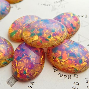 May include: Oval-shaped iridescent opal cabochons with a mix of orange, yellow, and green colors. The cabochons have a textured surface and a translucent appearance.