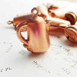May include: A collection of small copper-colored metal coffee pot charms. The charms are detailed and have a vintage look.