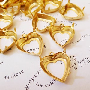 May include: A group of gold-colored heart-shaped metal settings for jewelry making. The settings have a smooth, shiny finish and are designed to hold a variety of gemstones or other decorative elements.