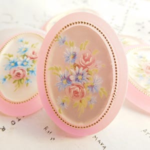 May include: Four pink oval-shaped decorative items with gold trim and floral designs. Each oval has a clear center with a painted floral design.