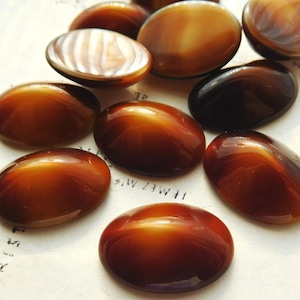 May include: A collection of oval-shaped buttons in shades of brown and amber. The buttons have a glossy, polished finish, with some revealing a pearlescent interior. These vintage buttons are ideal for sewing and craft projects.