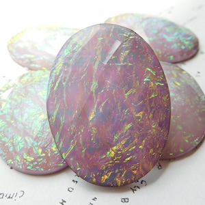 May include: Oval-shaped, iridescent cabochons in shades of pink, purple, and green. The polished stones have a glossy finish and are arranged on a white surface. The cabochons are likely used for jewelry making or other craft projects.