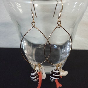 Puede incluir: Aretes de aro de oro con conchas marinas blancas y negras y detalles de coral colgando de la parte inferior.