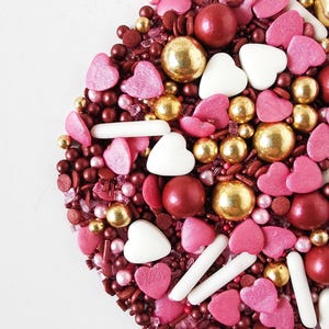 Peut inclure: Un assortiment de vermicelles en forme de cœur dans des tons de rose, rouge et or. Les vermicelles comprennent de petits cœurs, des boules rondes et de longs bâtonnets fins.