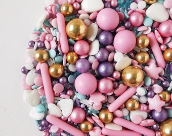 May include: A variety of colorful sprinkles, including pink, purple, gold, and blue, in the shape of hearts, stars, balls, and sticks.