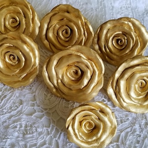 May include: Seven gold-colored rose-shaped decorations. The roses are made of a smooth, shiny material and have a realistic appearance.