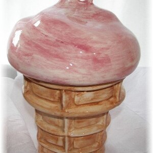 May include: A ceramic ice cream cone with a pink swirl on top. The cone is painted to look like a waffle cone.
