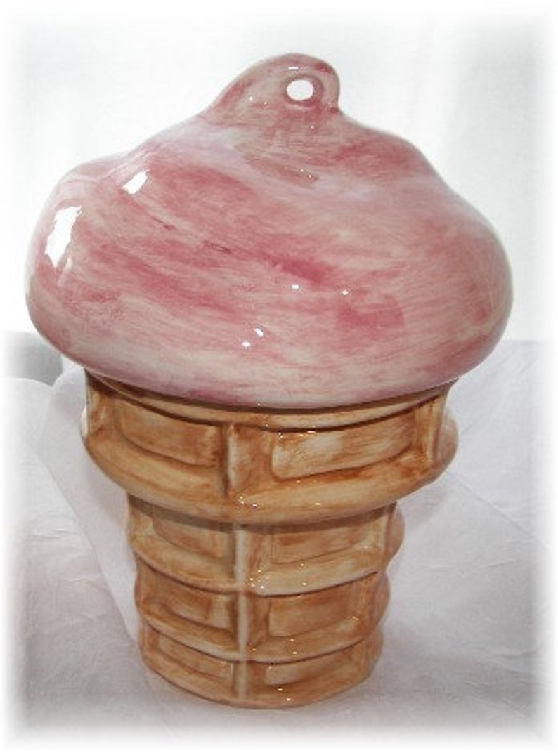 May include: A ceramic ice cream cone with a pink swirl on top. The cone is painted to look like a waffle cone.