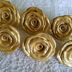 May include: Six gold-colored rose-shaped decorative drawer pulls. The pulls are made of a smooth, shiny material and have a realistic rose design.