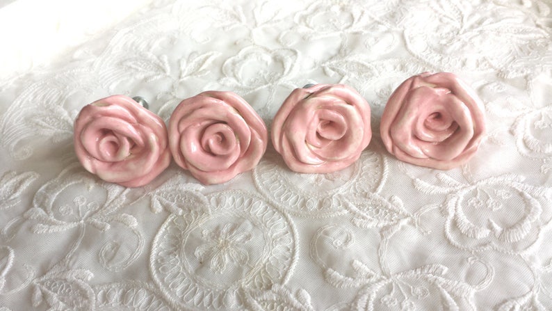 K&ouml;nnte beinhalten: Vier rosafarbene Keramik-Schubladengriffe in Rosenform mit silberner Beschl&auml;ge.