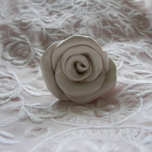 Peut inclure: Une rose en céramique blanche avec un motif en spirale, posée sur un tissu en dentelle blanche.