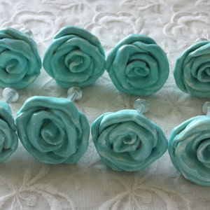May include: Eight turquoise ceramic rose-shaped drawer pulls. Each pull has a white center and a raised design.
