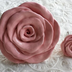 Könnte beinhalten: Zwei rosafarbene Keramik-Rosen-Schubladengriffe. Die größere Rose hat einen Durchmesser von etwa 10 cm. Die kleinere Rose hat einen Durchmesser von etwa 5 cm.