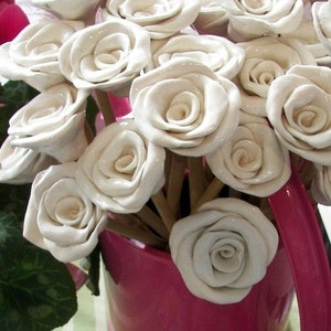 May include: A bouquet of white ceramic roses arranged in a pink watering can. The roses are crafted with intricate details and have a delicate, vintage aesthetic.