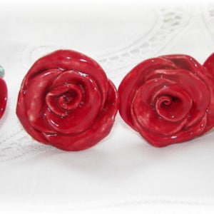 以下が含まれることがあります： バラの形をした赤いセラミック製の引き出しノブが4つ。ノブは光沢があり、リアルなバラのデザインです。