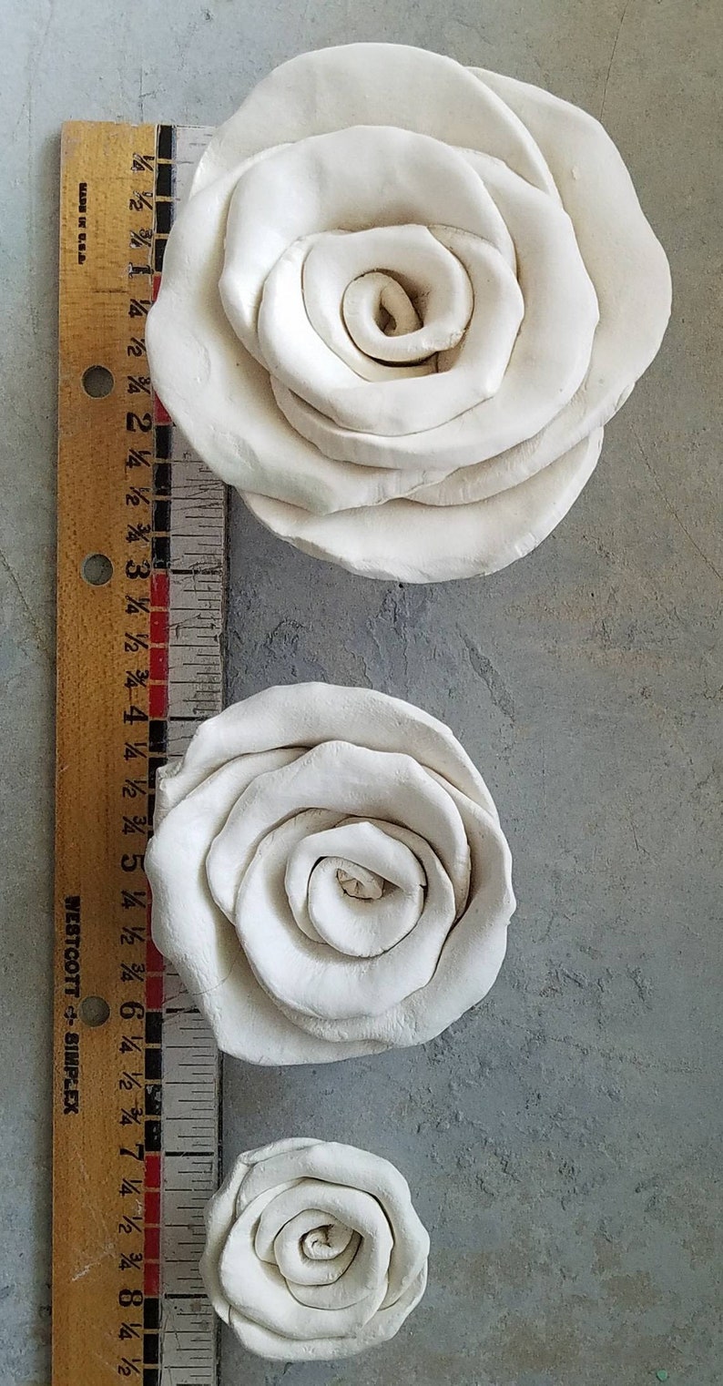 以下が含まれることがあります： 3 つの異なるサイズの白い粘土のバラ。バラは、一番大きいバラが画像の上部にくるように、大きい順に並んでいます。バラはすべて白い粘土でできており、滑らかで磨かれた仕上げになっています。
