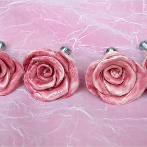 Puede incluir: Cuatro tiradores de cajón de cerámica rosa en forma de rosa con herrajes de metal plateado.
