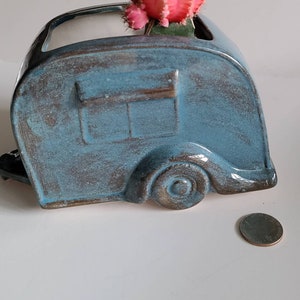 May include: A blue ceramic planter shaped like a vintage camper with a pink cactus plant inside.