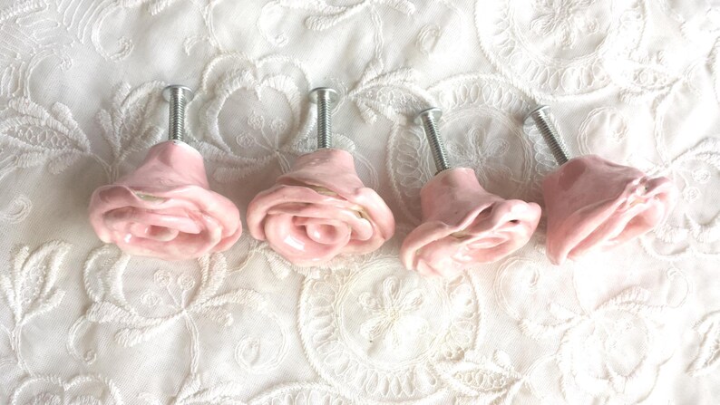 以下が含まれることがあります： 銀色の金属製の茎が付いた、ピンクのセラミック製のバラの形をした引き出しの取っ手が4つ。