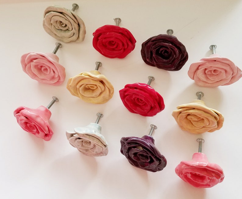 May include: Assortment of 12 ceramic rose drawer pulls in various colors, including pink, red, cream, and purple. Each pull features a 3D rose design with a silver metal screw.