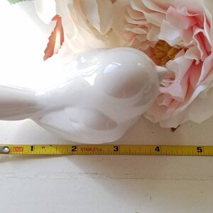 May include: A white ceramic bird figurine with a rounded body and a long, curved beak. The bird is approximately 4 inches long and is sitting on a white surface.