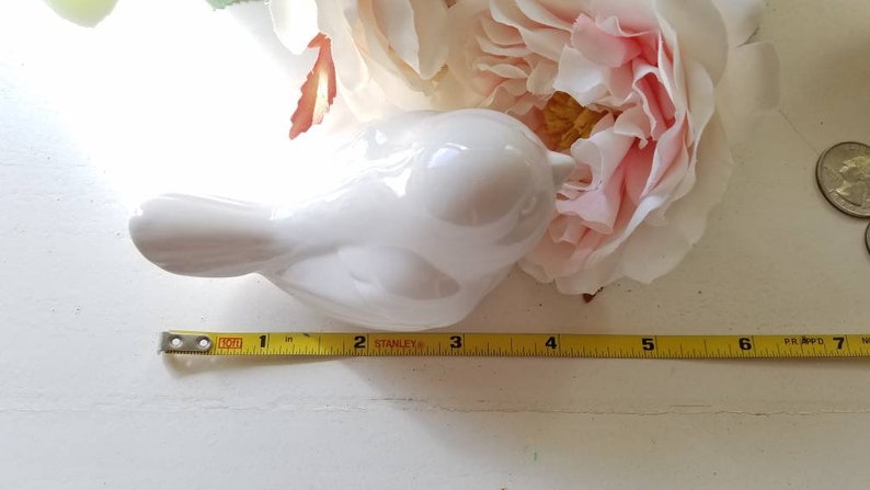 May include: A white ceramic bird figurine with a rounded body and a long, curved beak. The bird is approximately 4 inches long and is sitting on a white surface.
