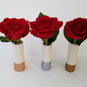 May include: Three small white ceramic vases with gold and silver accents, each holding a single red rose.