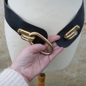 May include: A black leather belt with a gold metal buckle. The buckle is a large, intricate design with multiple loops and curves.