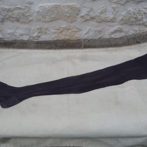 Peut inclure: Un bas-cuisse unique, gris foncé, est posé sur une surface blanche. Le bas est fait d'une matière transparente et est conçu pour s'étendre bien au-dessus du genou. Le bas est posé à plat, mettant en valeur sa longueur et sa forme.