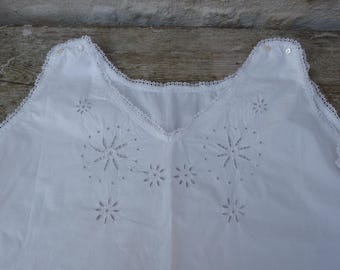 Puede incluir: Prenda de algodón blanco con cuello en V y patrones decorativos de estrellas y flores recortadas. El escote y los bordes están adornados con delicado encaje. Se ven dos pequeños botones en la zona del hombro.