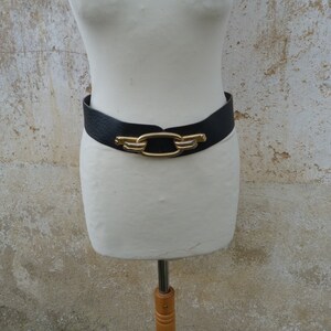 May include: A black leather belt with a gold-toned buckle featuring a large oval link design.
