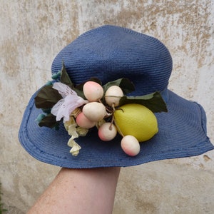 May include: A blue sun hat with a lemon and white flowers on top.