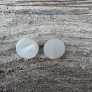 Peut inclure: Deux boutons ronds blancs avec un éclat nacré. Les boutons ont une tige métallique argentée au dos.