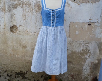 Puede incluir: Un vestido de vichy azul y blanco con un corpiño azul y ribete de encaje blanco. El vestido está en un maniquí de madera.