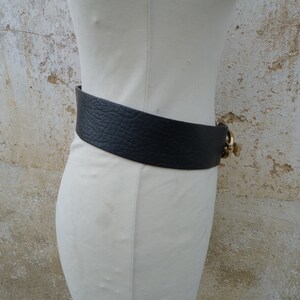 May include: A wide black leather belt with a gold buckle. The buckle has a decorative design.