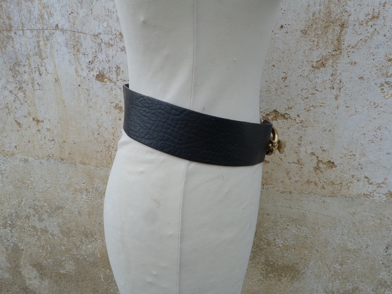 May include: A wide black leather belt with a gold buckle. The buckle has a decorative design.