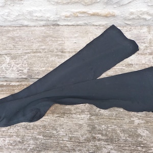 Puede incluir: Un par de calcetines negros opacos por encima de la rodilla hechos de una tela suave y elástica. Los calcetines presentan un color negro sólido en toda la prenda, con una sección de pie definida y una parte larga y recta para la pierna.